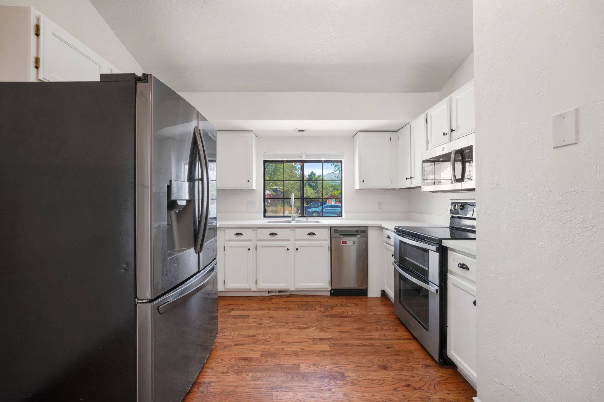 Kitchen featuring white cabinetry, wood-finish flooring, stainless steel appliances, a double oven range, and a window above the sink