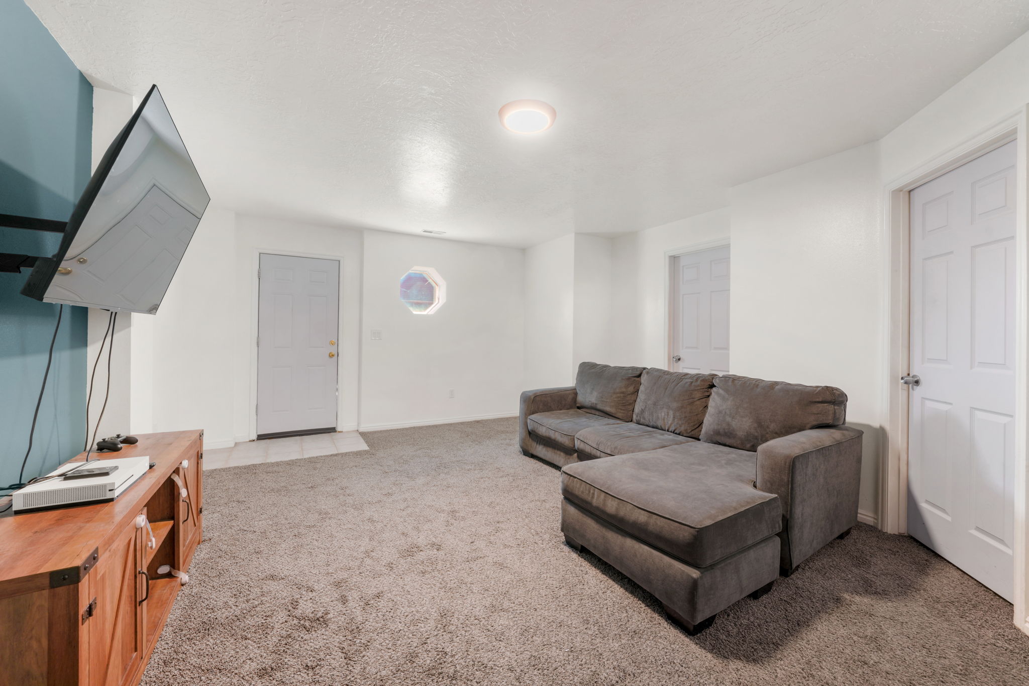 Carpeted room featuring a ceiling-mounted light fixture, white walls, and a distinct octagonal window
