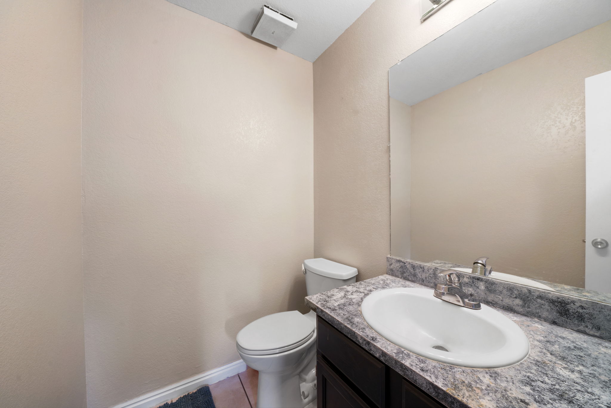 Bathroom featuring a dark wood-finish vanity with an integrated sink, patterned countertop, and chrome faucet