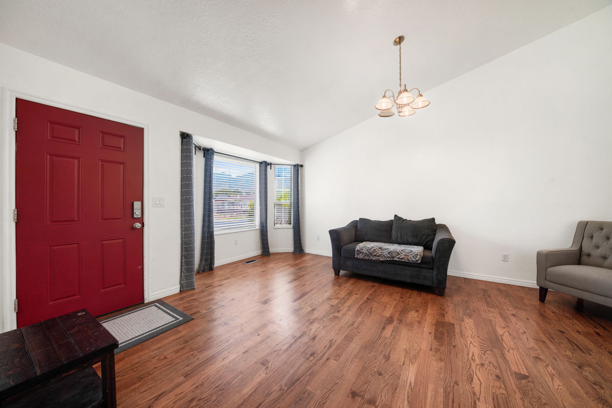 Entryway featuring a red paneled door with smart lock, wood-finish flooring, a bay window with blinds, and an overhead chandelier