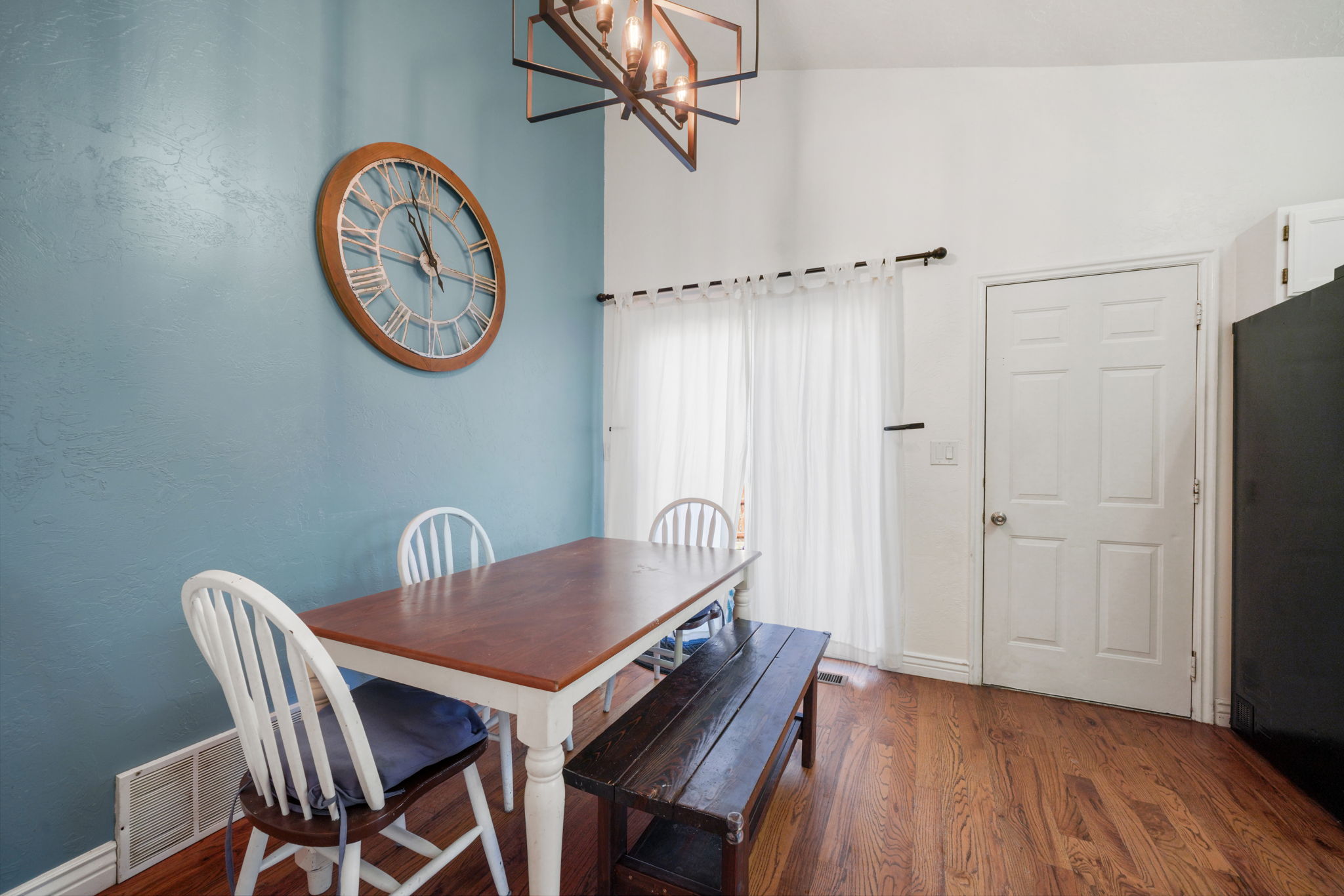 Dining area featuring hardwood flooring, a vaulted ceiling, a geometric chandelier, and a sliding glass door with white curtains