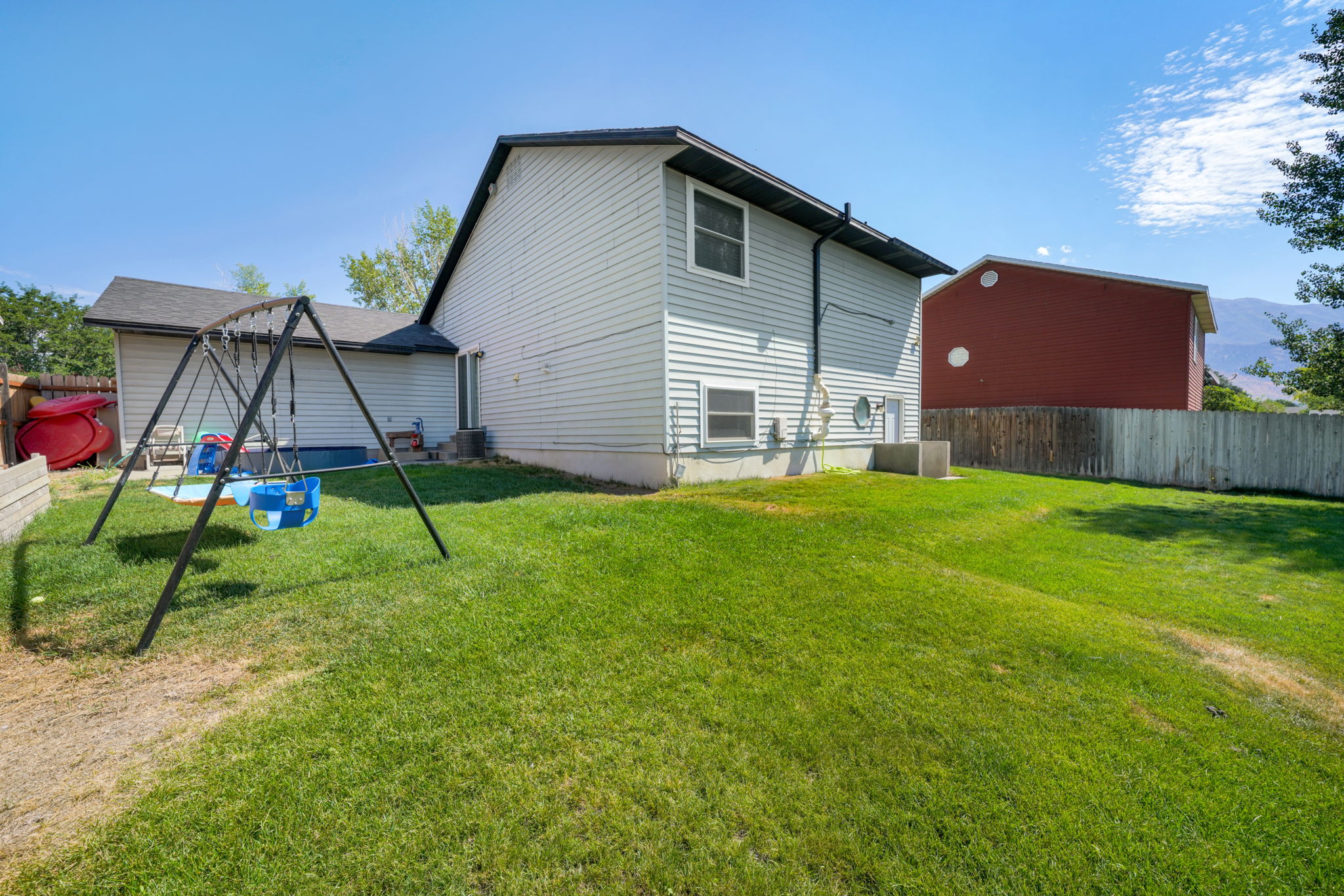 Spacious backyard with a vibrant green lawn, featuring a light-colored privacy fence and a two-story residence with light-toned siding