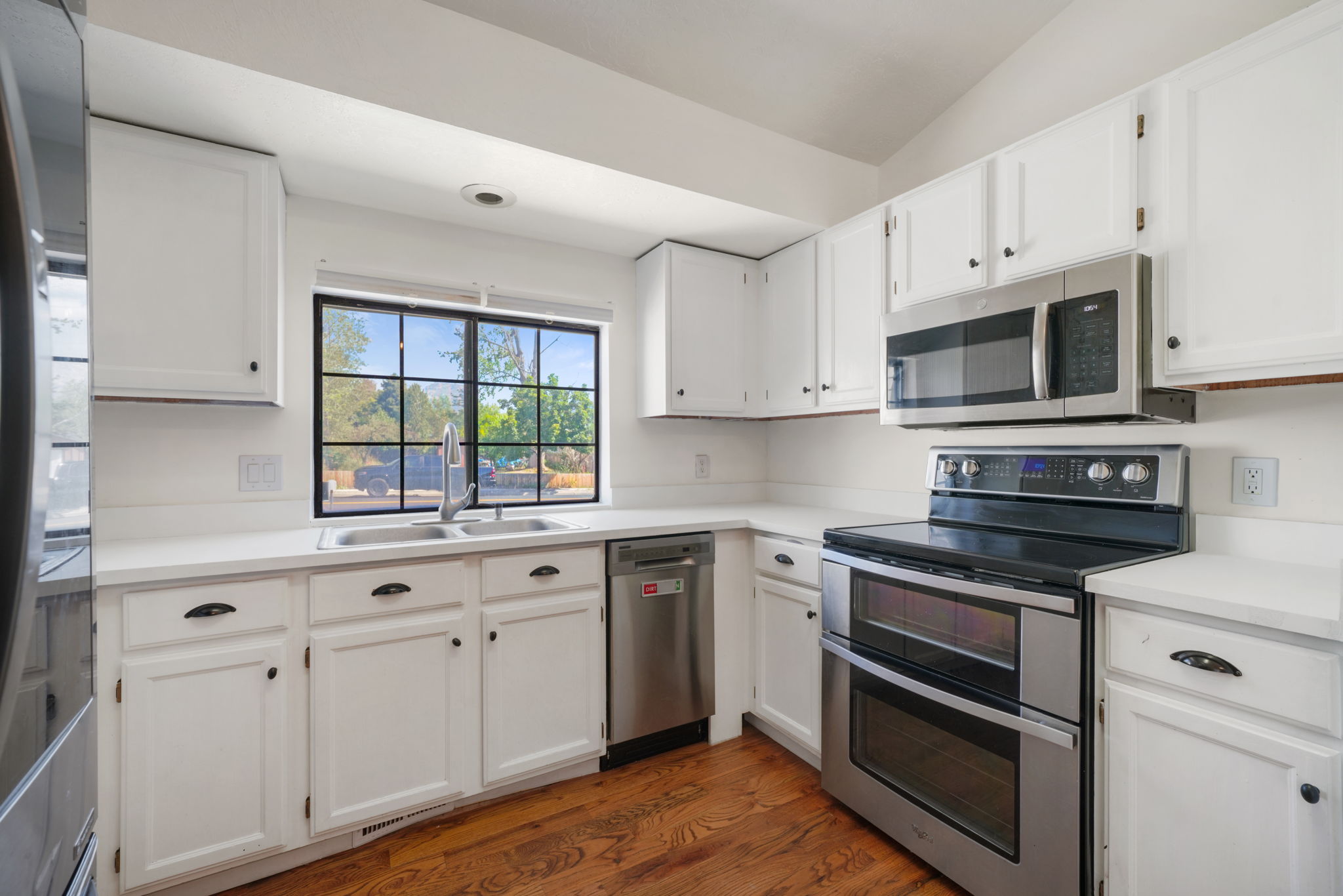 Kitchen featuring white cabinetry, light-toned countertops, stainless steel appliances, and wood-finish flooring