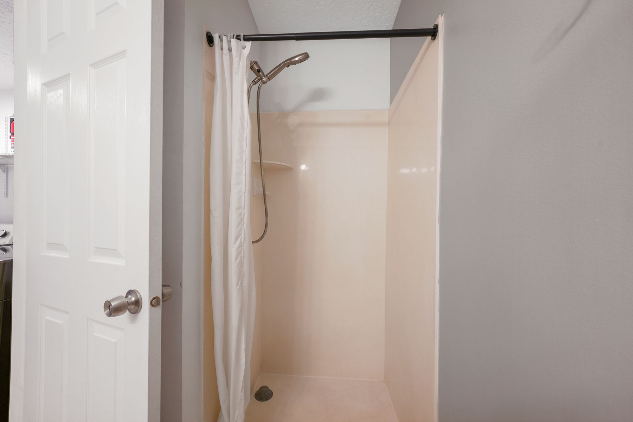 Enclosed shower with built-in shelving, a handheld showerhead, and a curtain rod
