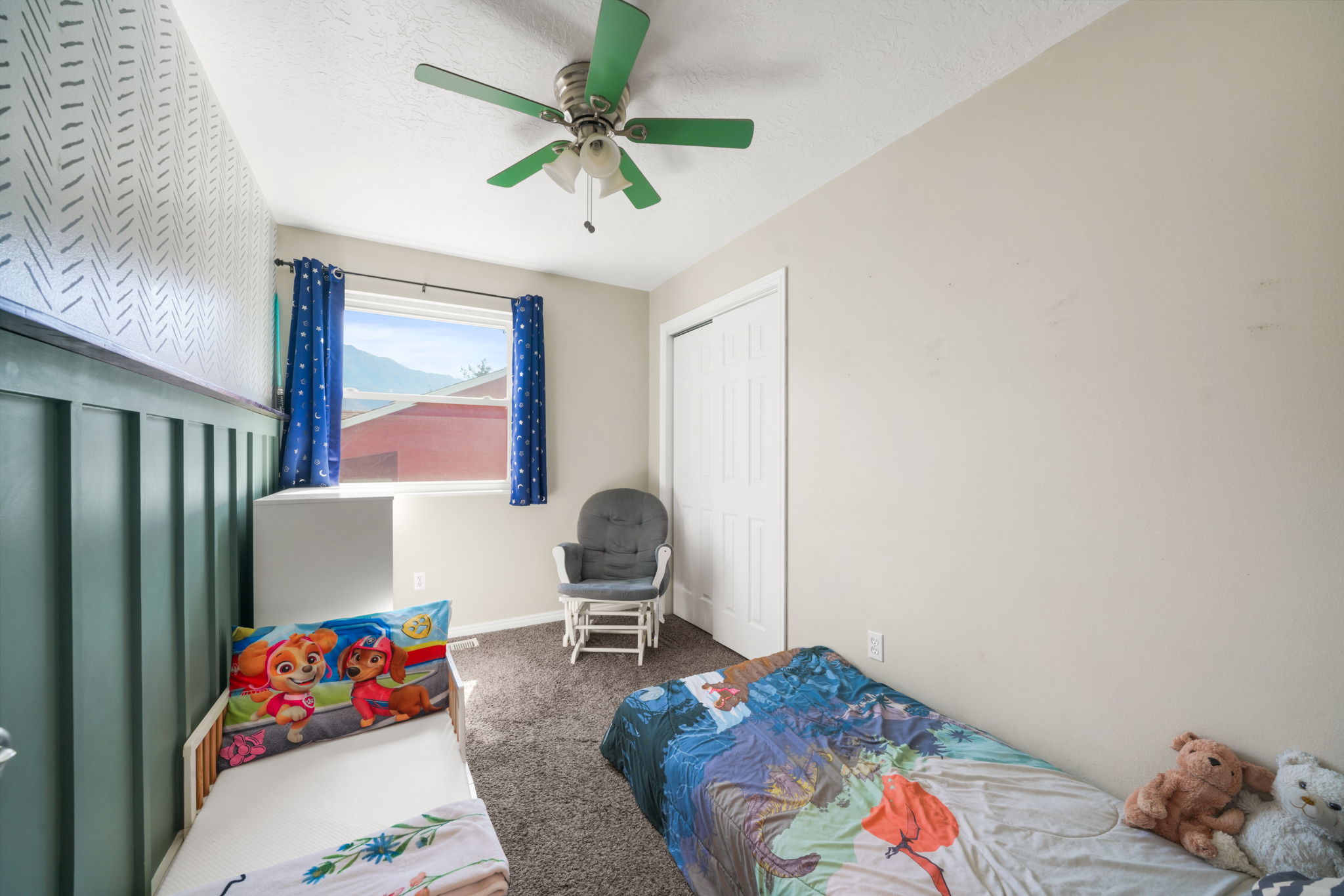 Room featuring a window with exterior mountain scenery, ceiling fan with integrated lighting, textured wall paneling, and neutral carpeting