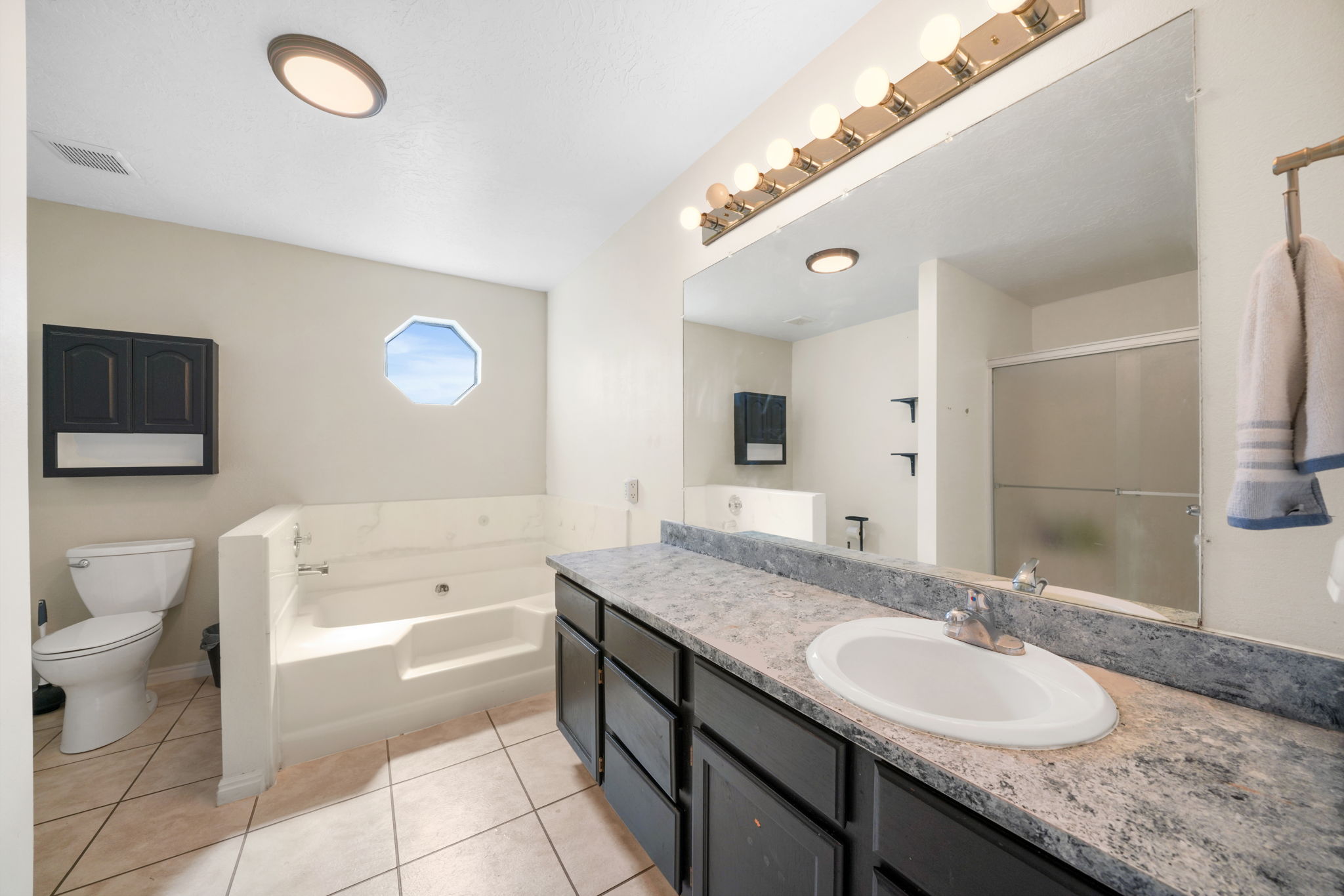 Bathroom featuring a built-in tub with steps, octagonal window, and a vanity with an integrated sink