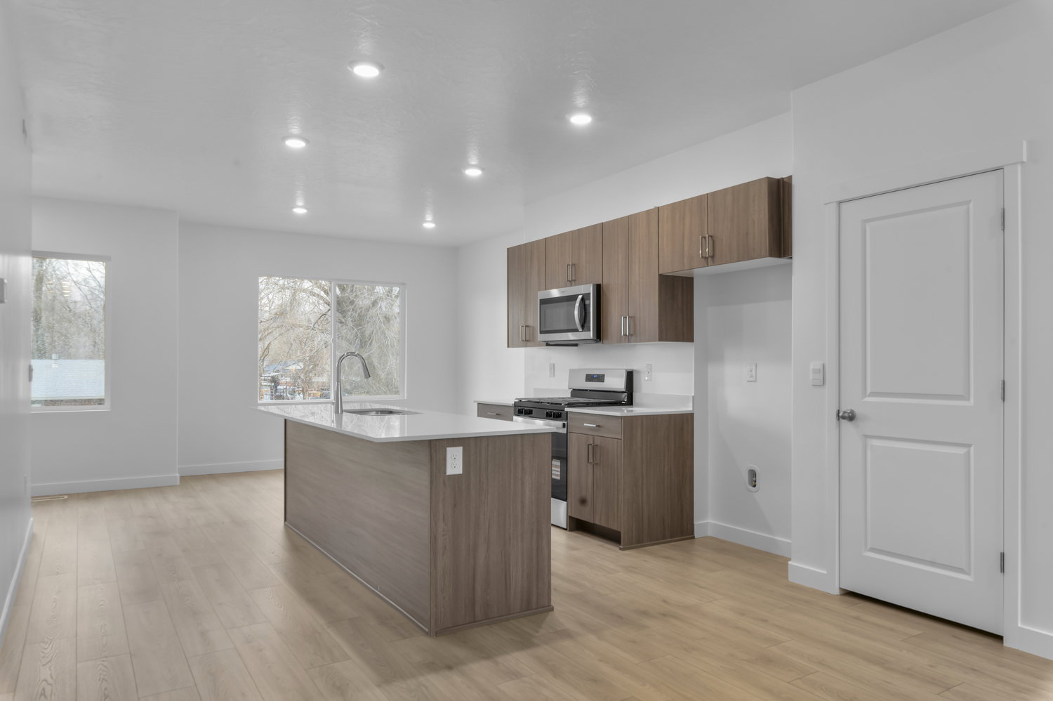Open-concept living area featuring wood-finish flooring, recessed lighting, and a kitchen with wood-look cabinetry, a center island with sink, and stainless steel appliances