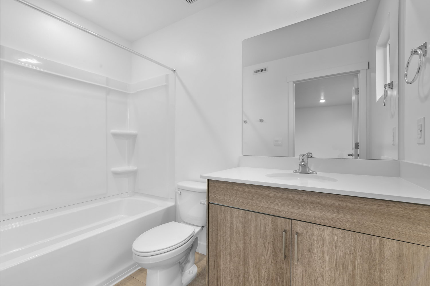 Bathroom featuring a white tub-shower combination with integrated shelving, a sleek toilet, and a vanity with a white countertop and wood-finish cabinetry