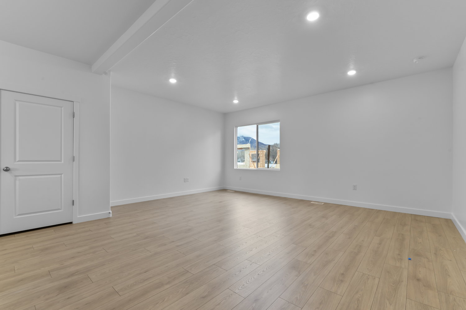 Spacious interior room featuring light wood-finish flooring, recessed lighting, white walls, white trim, and a window offering a mountain backdrop