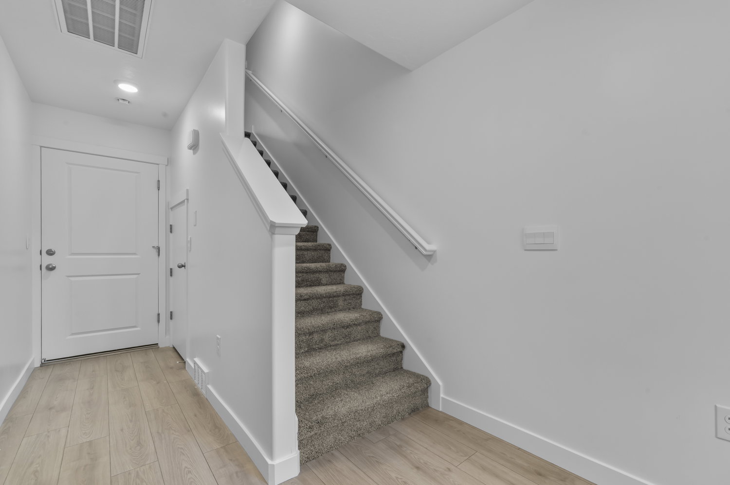 Entrance foyer featuring wood-finish flooring and a carpeted staircase with a white handrail