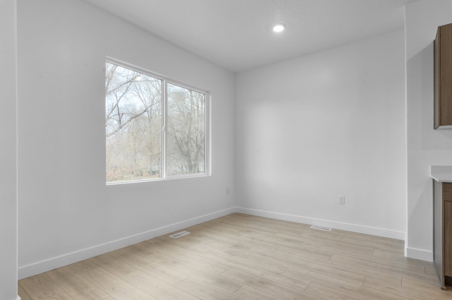 Bright interior space featuring a large window with white framing, wood-finish flooring, recessed lighting, and white baseboards