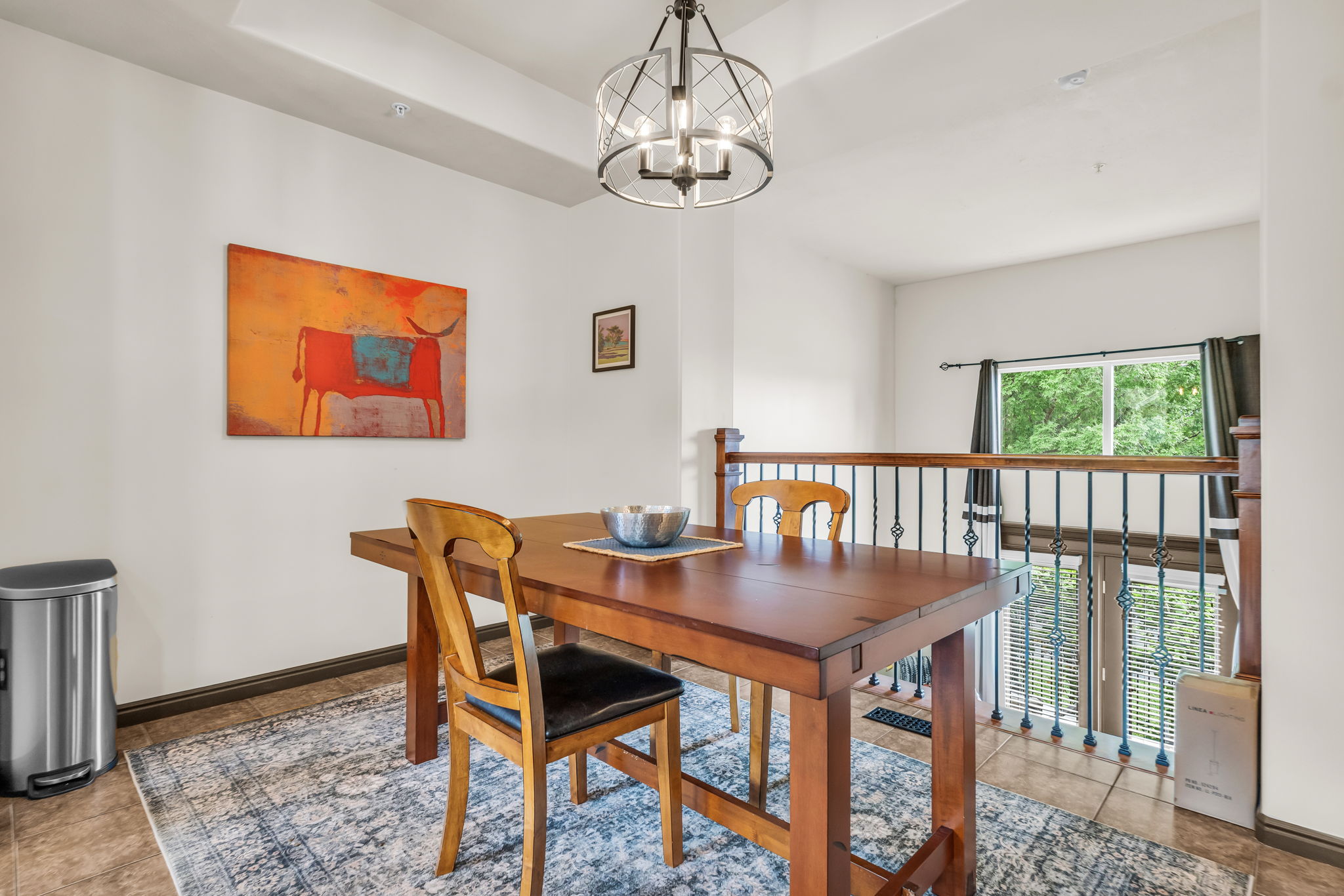 Dining area featuring a decorative chandelier, tile flooring, and a wrought iron banister overlooking the floor below