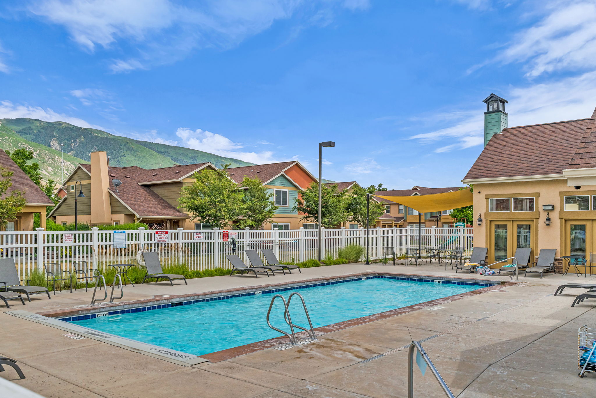 Rectangular outdoor pool with concrete surround, white perimeter fencing, and a nearby building featuring a cupola