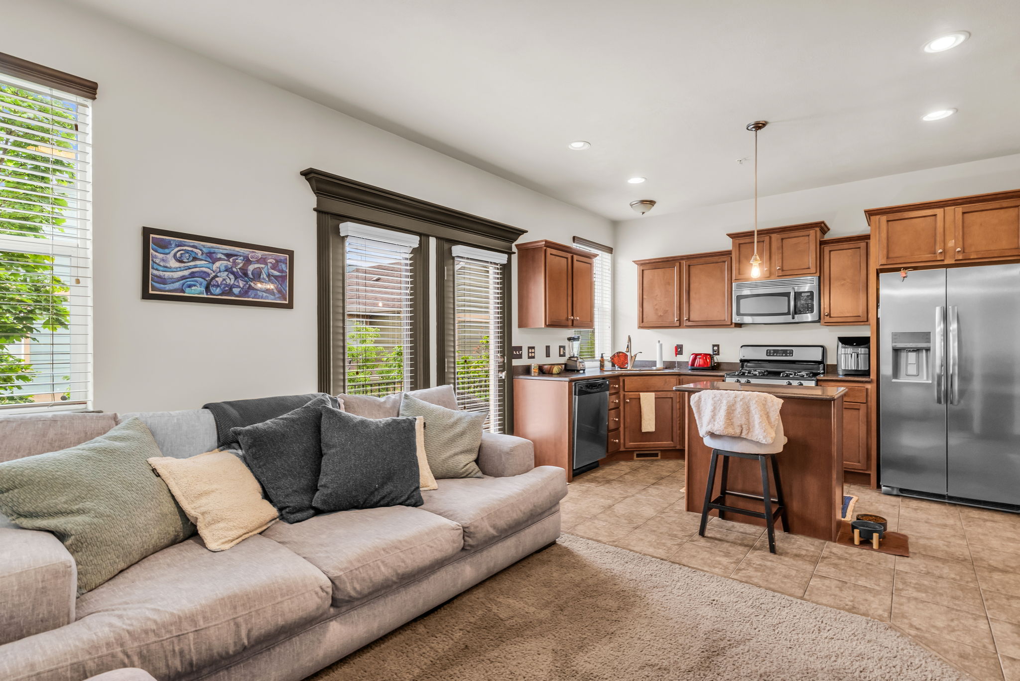 Open-concept living space featuring wood-finish cabinetry, stainless steel appliances, recessed lighting, and a kitchen island with pendant light