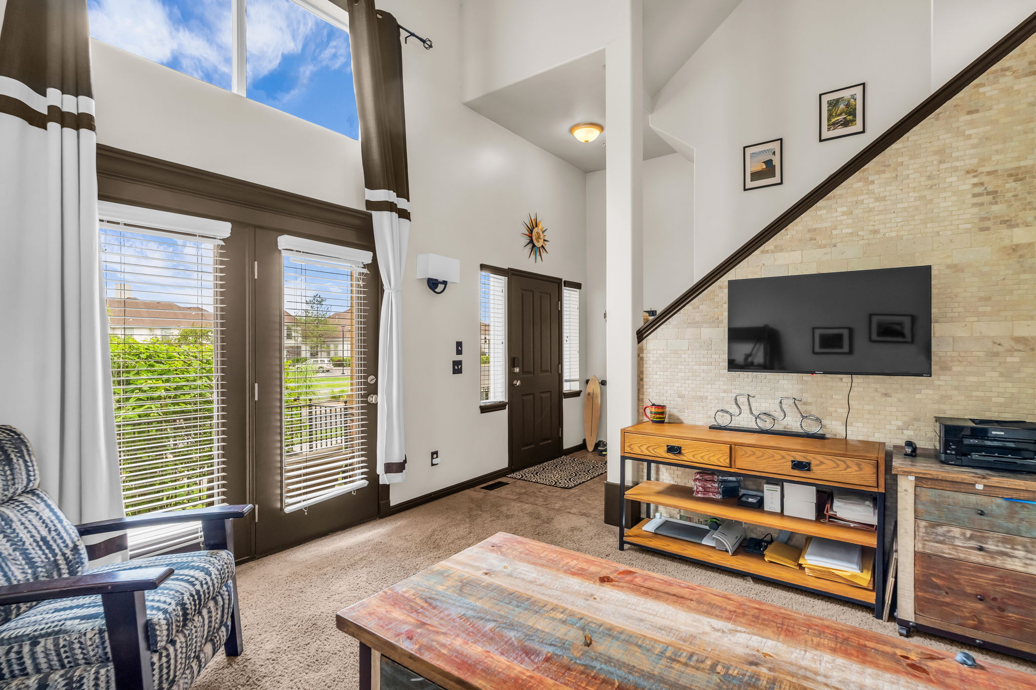Vaulted ceiling living area featuring double French doors, transom windows and a textured accent wall.