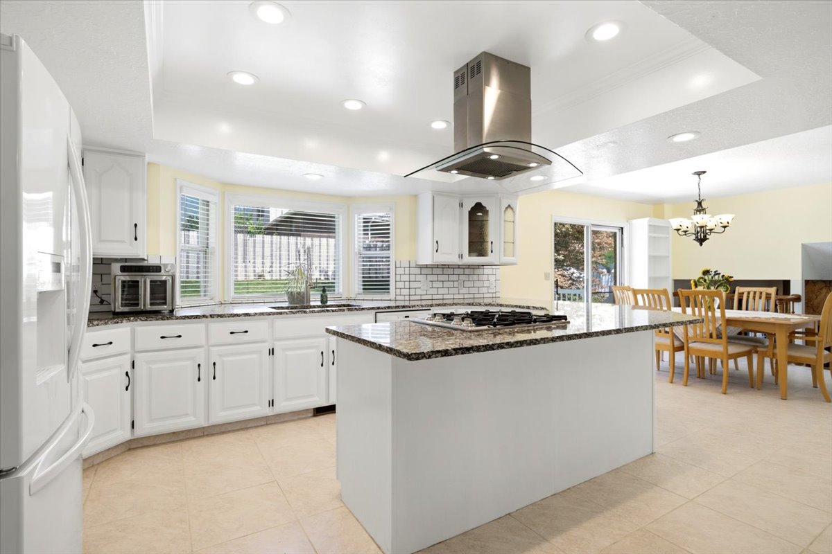 Kitchen featuring a central island with a built-in cooktop, white cabinetry, speckled countertops, and a subway tile backsplash