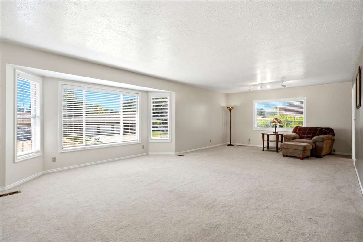 Spacious living area featuring light-colored carpeting, multiple windows with horizontal blinds, and a large bay window