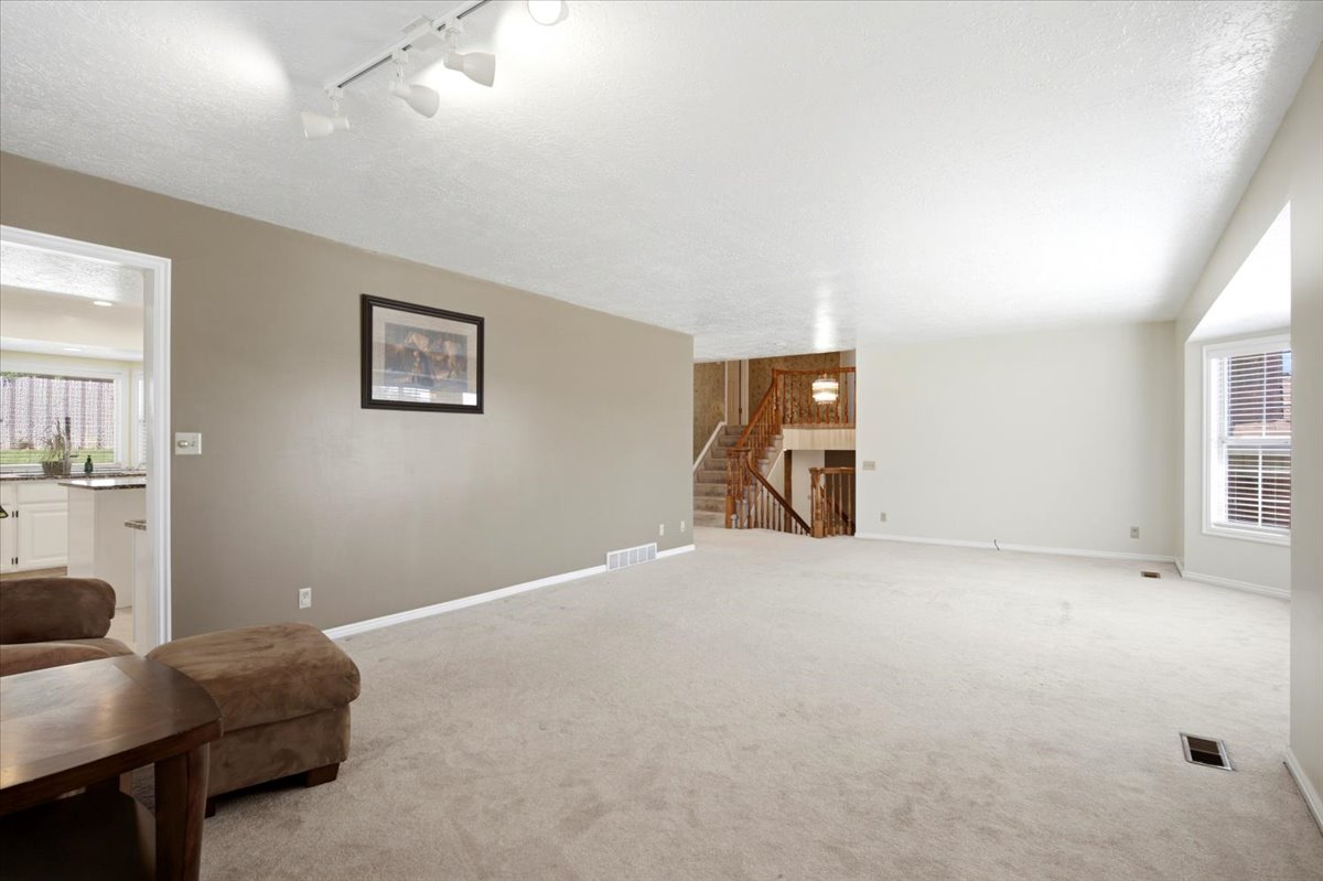 Carpeted living area featuring track lighting, a bay window with blinds, and a staircase with wood railing