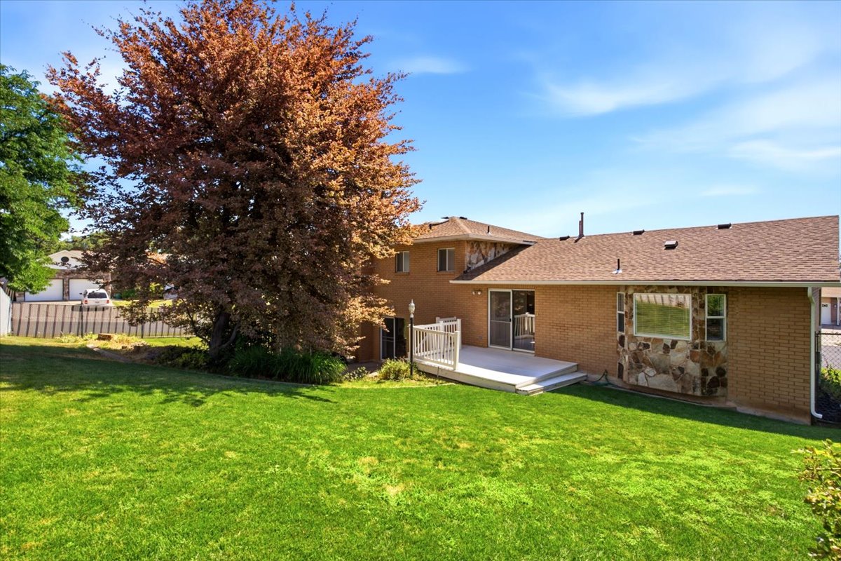Expansive rear yard with a large tree, a raised deck with white railings, and a brick exterior with stone accenting