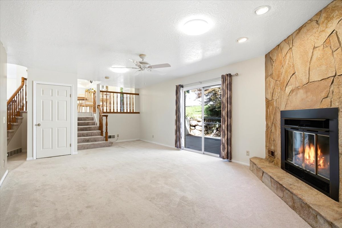 Spacious living area featuring a floor-to-ceiling stone fireplace, ceiling fan, recessed lighting, and sliding glass door access to the outdoor space