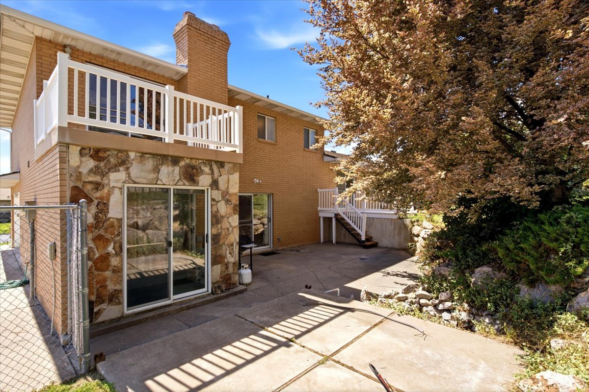 Rear exterior featuring a concrete patio, brick and stone facade, and upper-level balcony with white railings