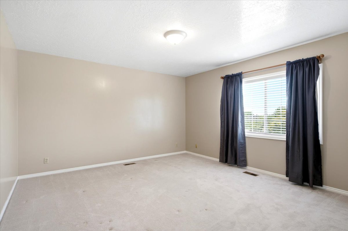 Spacious room featuring neutral carpeting, light beige wall paint, and a single window with white blinds