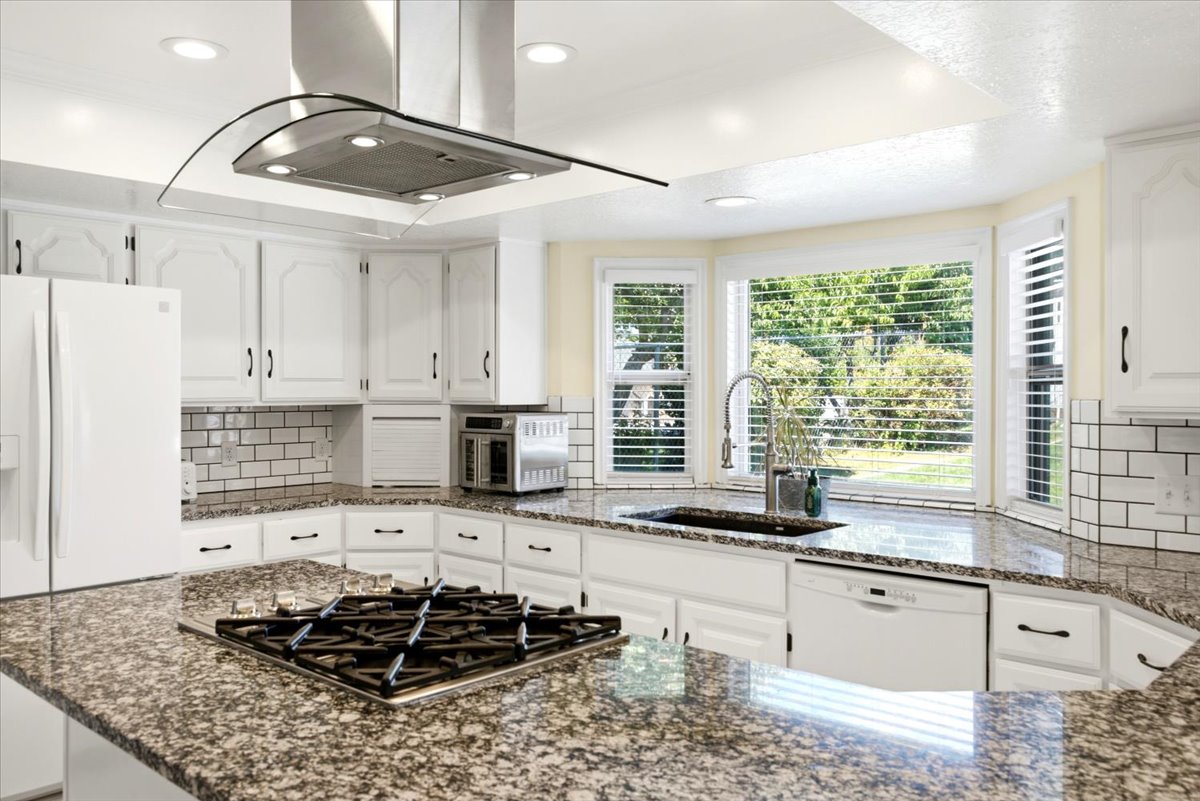 Contemporary kitchen featuring white cabinetry, granite countertops, subway tile backsplash, and a built-in gas range with an overhead vent hood