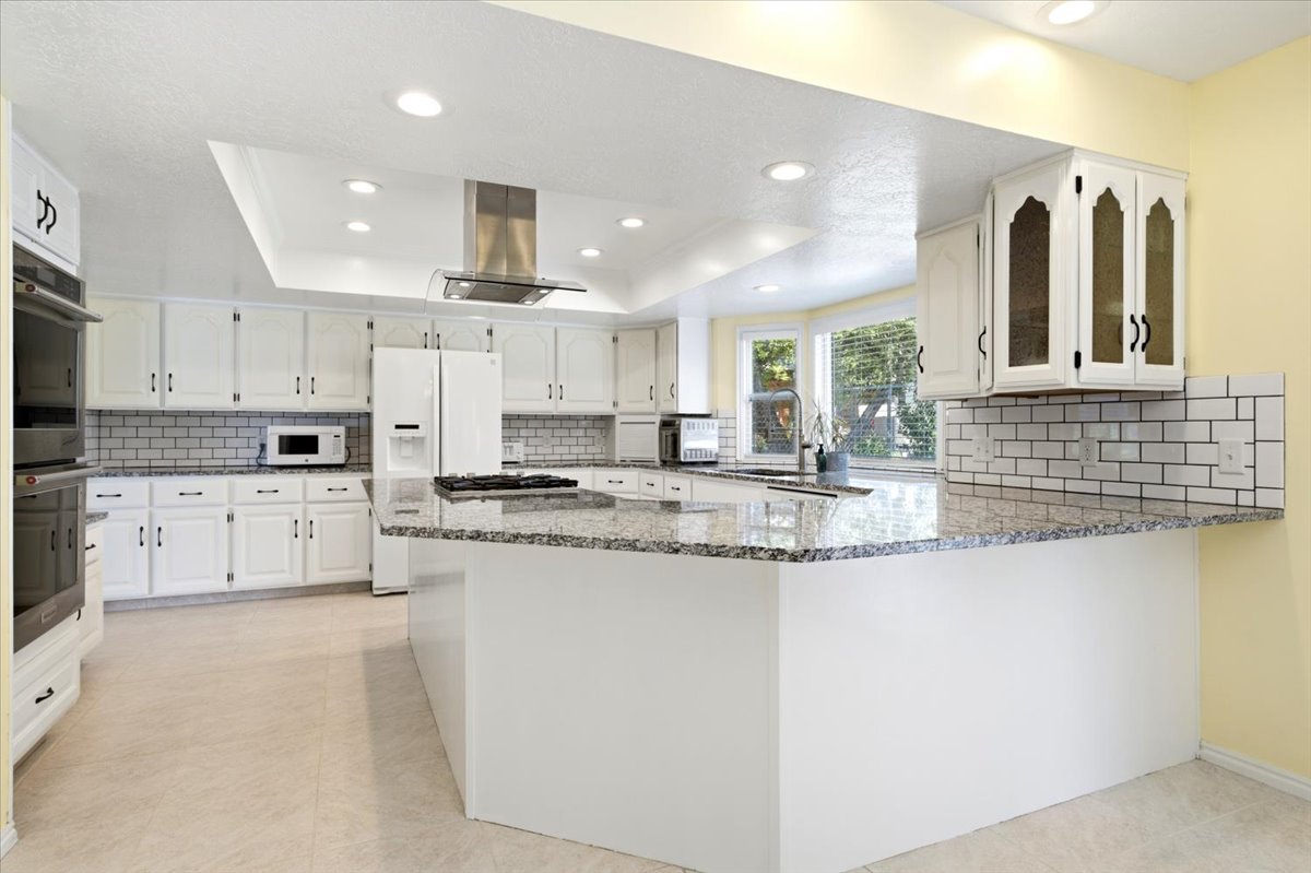 Spacious kitchen featuring an expansive island with granite countertops, abundant white cabinetry, subway tile backsplash, and recessed lighting