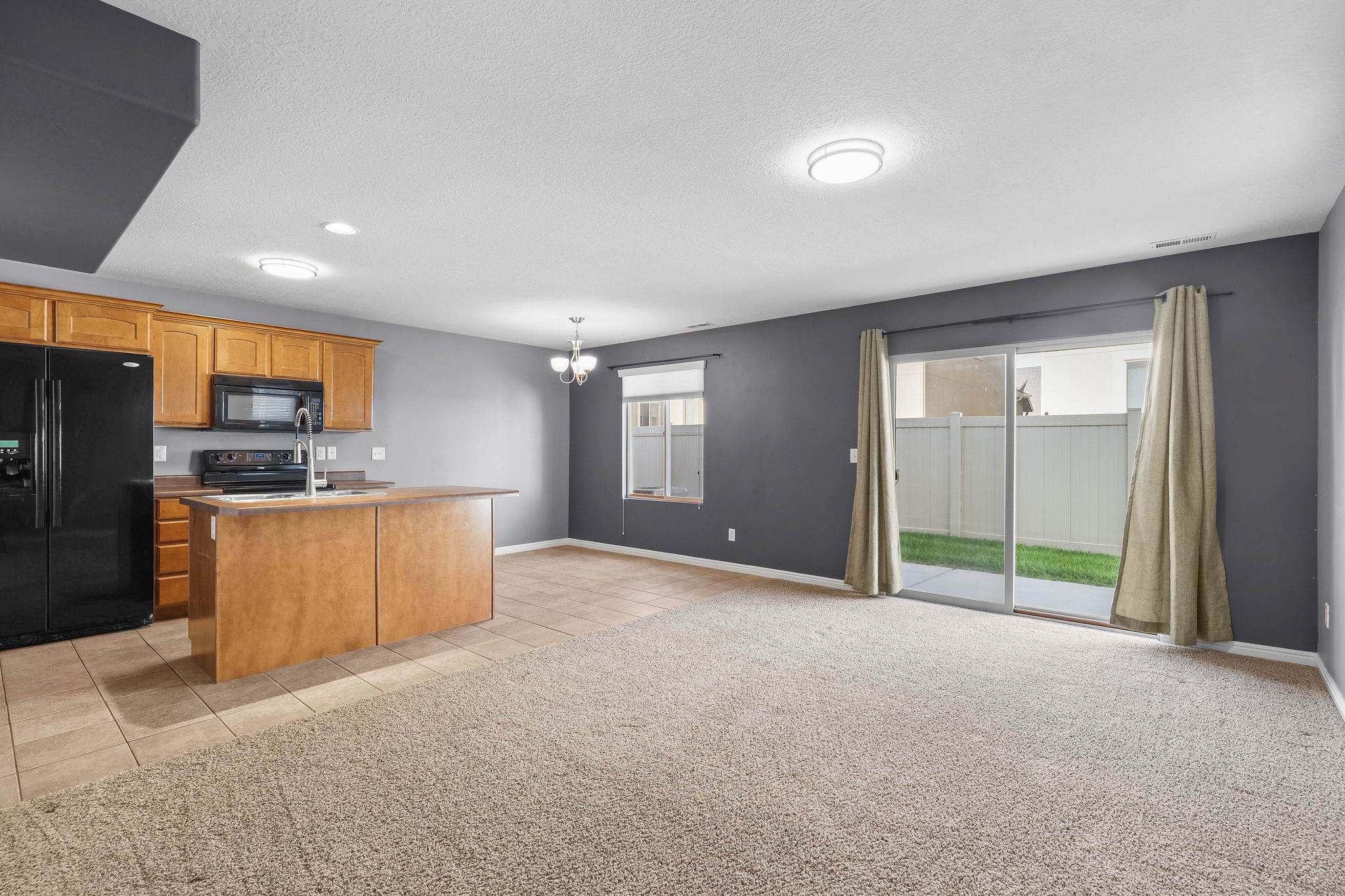 Kitchen and living area featuring dark gray walls, light wood cabinetry, black appliances, and a central island