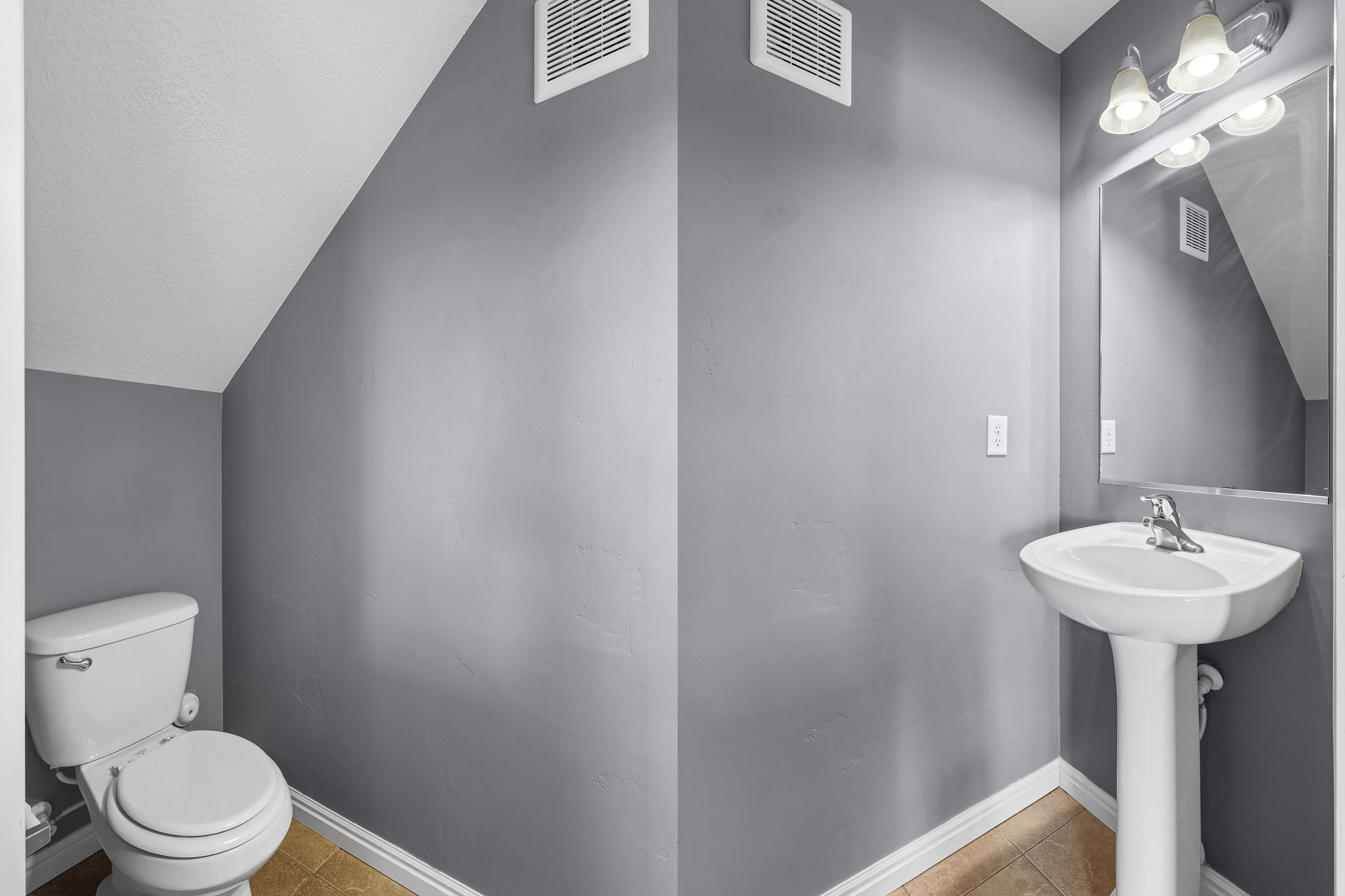 Powder room featuring a pedestal sink with chrome faucet, wall-mounted mirror, and a three-light vanity fixture