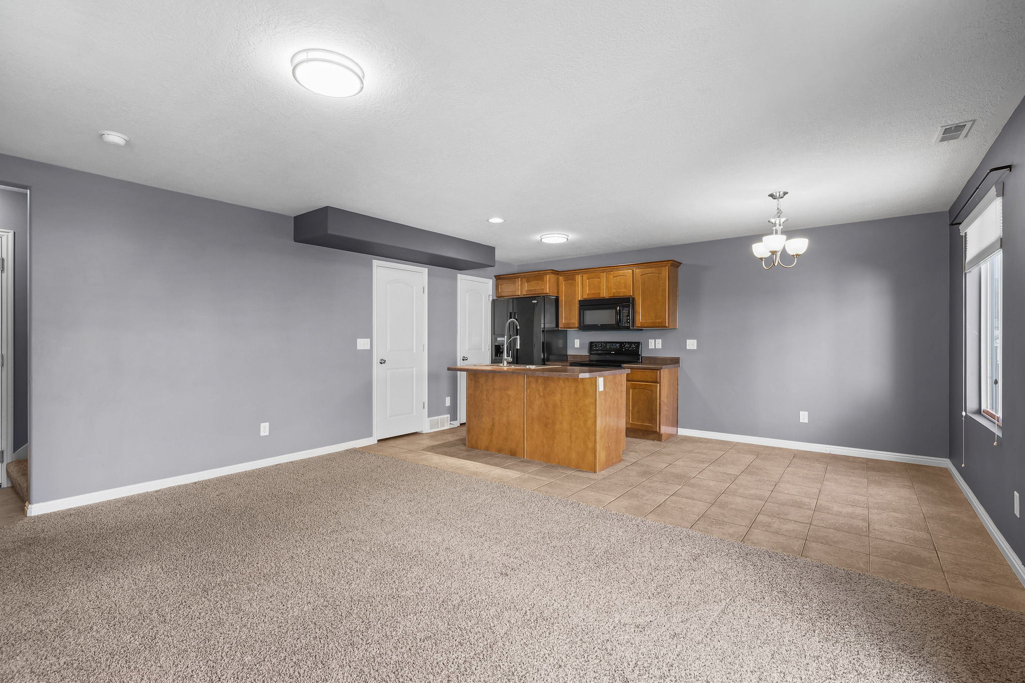 Open-concept living space featuring a kitchen with wood cabinetry, black appliances, and a central island