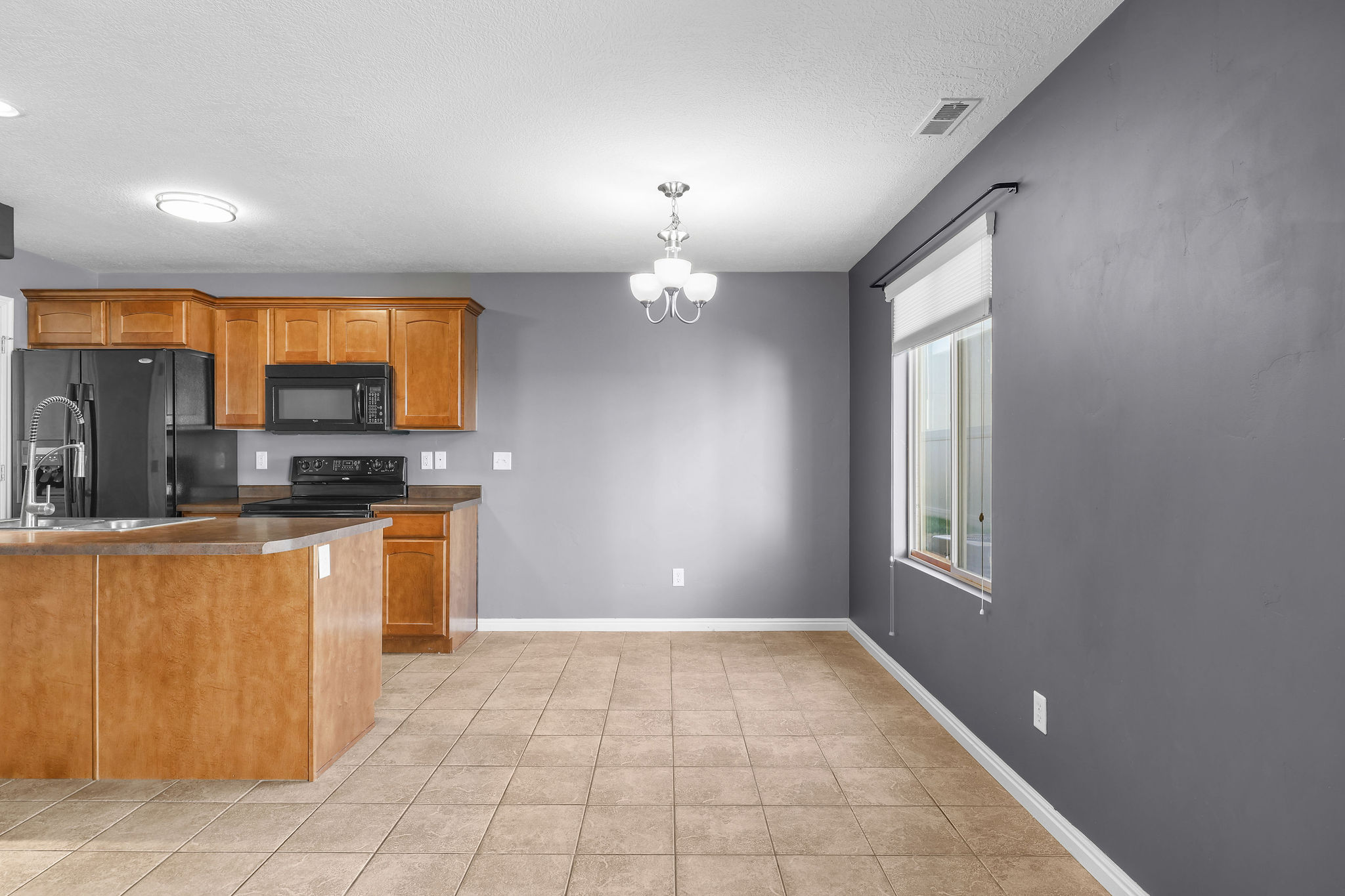 Kitchen and dining area featuring warm wood cabinetry, black appliances, tile flooring, and a modern chandelier