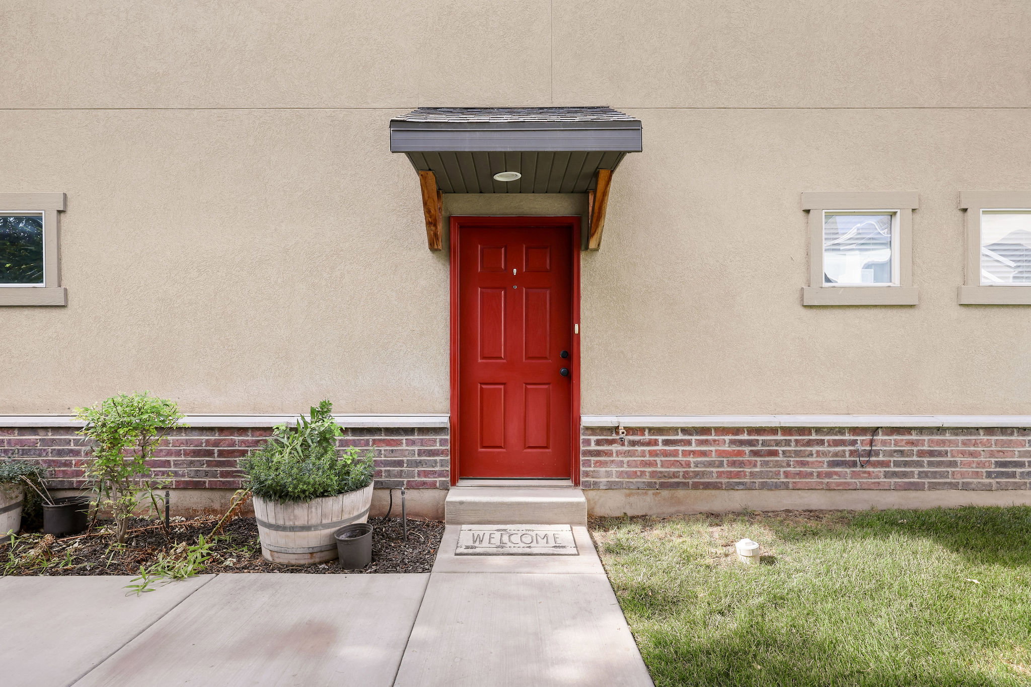 Red paneled entry door with an overhead awning, stucco exterior, and a brick accent foundation