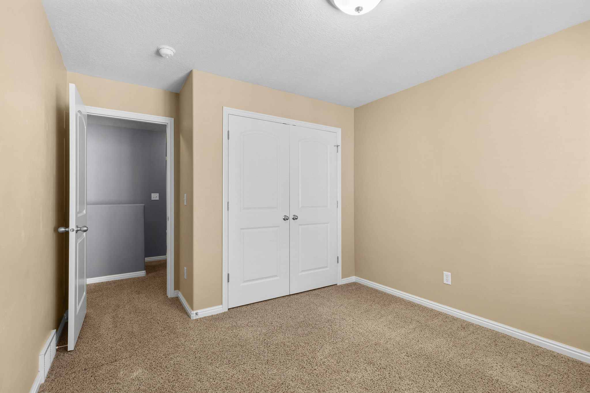 Bedroom featuring neutral-toned carpet flooring, light beige wall paint, white baseboards, and a double-door closet with arch paneling