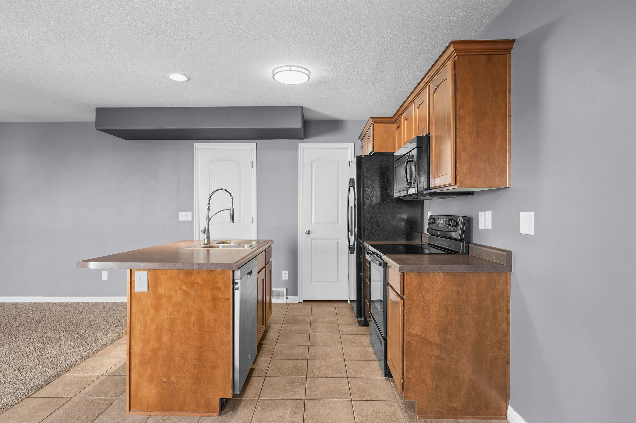 Kitchen featuring wood-finish cabinetry, black appliances, a central island with a double basin sink, and tile flooring