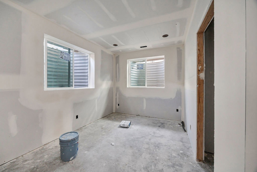 Room under construction featuring two egress windows with white vinyl frames, drywall-finished walls, a concrete subfloor, and an unfinished doorway opening