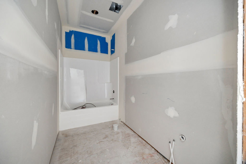 Bathroom space under construction featuring a built-in tub and shower unit, prepared drywall, exposed electrical wiring, and plumbing rough-ins