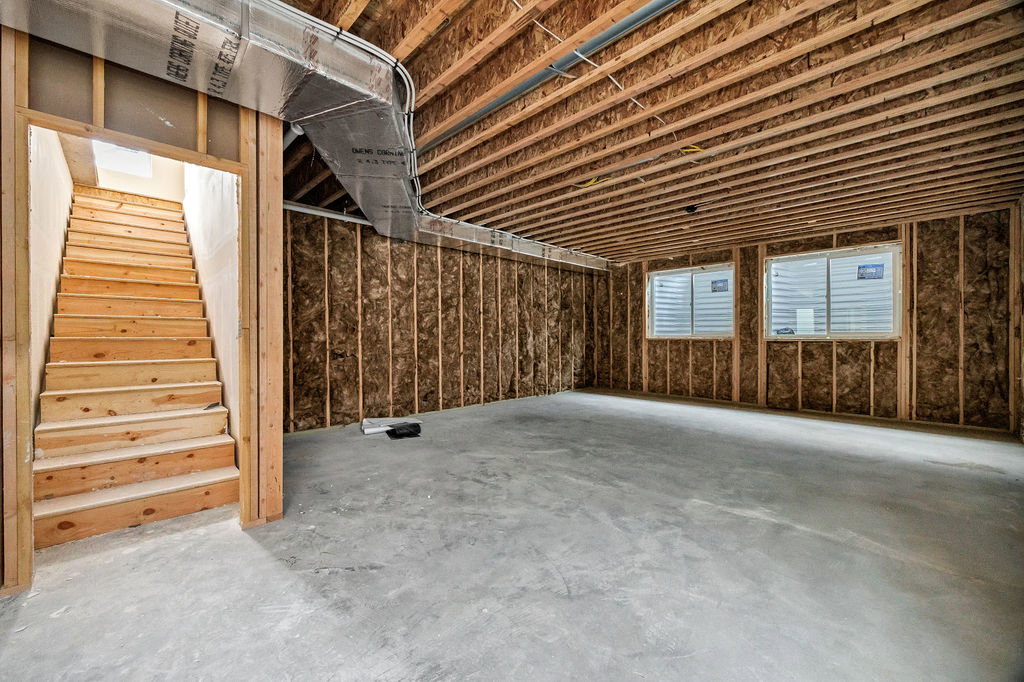 Unfinished basement space featuring exposed wood framing, uninsulated wall sections, and two visible windows