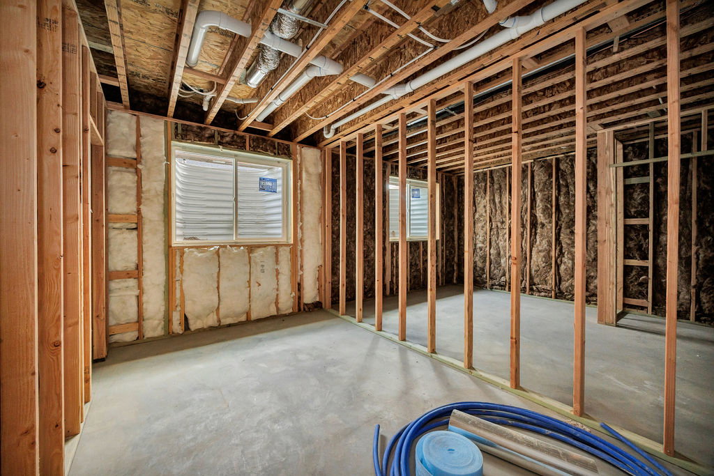Unfinished basement space featuring visible wood framing, concrete flooring, and an exposed ceiling with plumbing