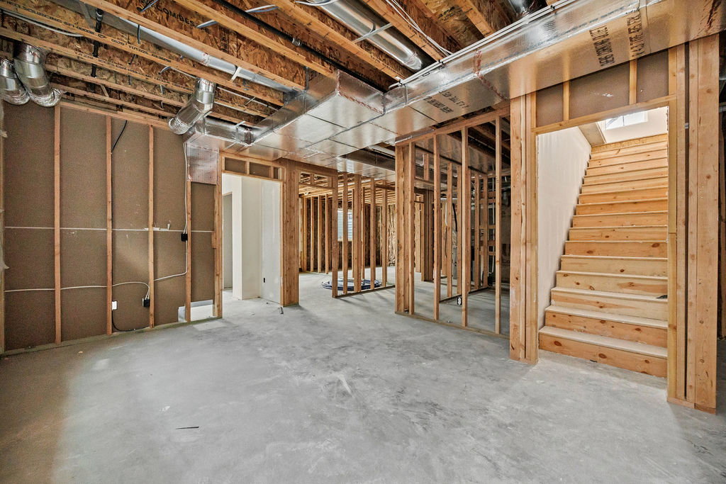 Unfinished basement featuring wood framing, exposed ceiling joists, concrete flooring, and an open wooden staircase