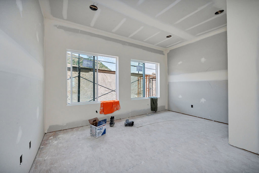 Unfinished interior room featuring two large windows, recessed lighting, and a tray ceiling