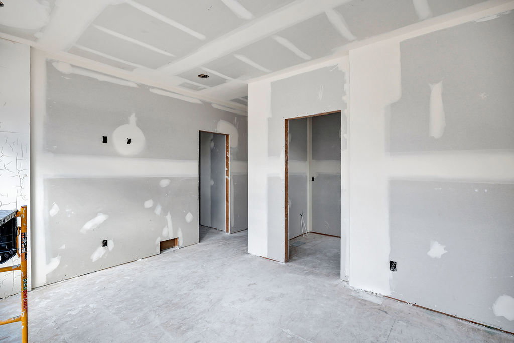 Interior space under construction featuring drywall installation, unfinished ceilings, and exposed door frames