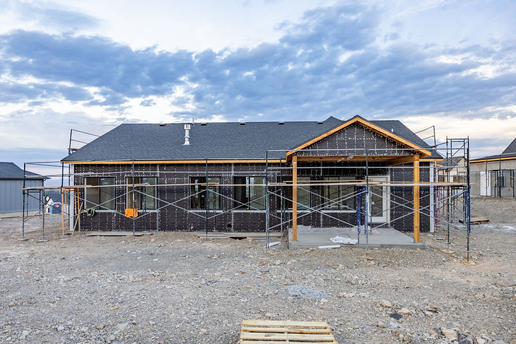 Rear exterior of a new construction residence featuring a dark shingle roof and multiple windows
