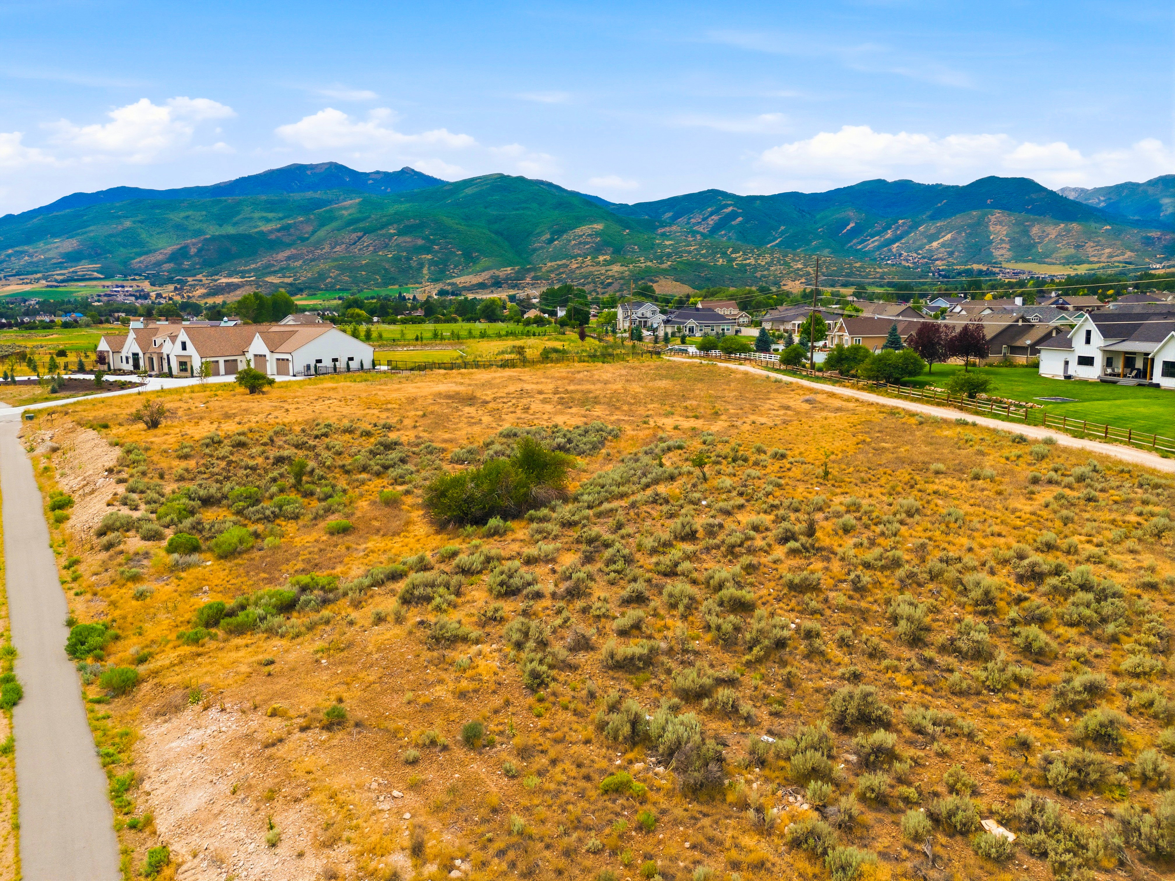 Expansive land parcel featuring natural shrubbery and a paved road bordering the property
