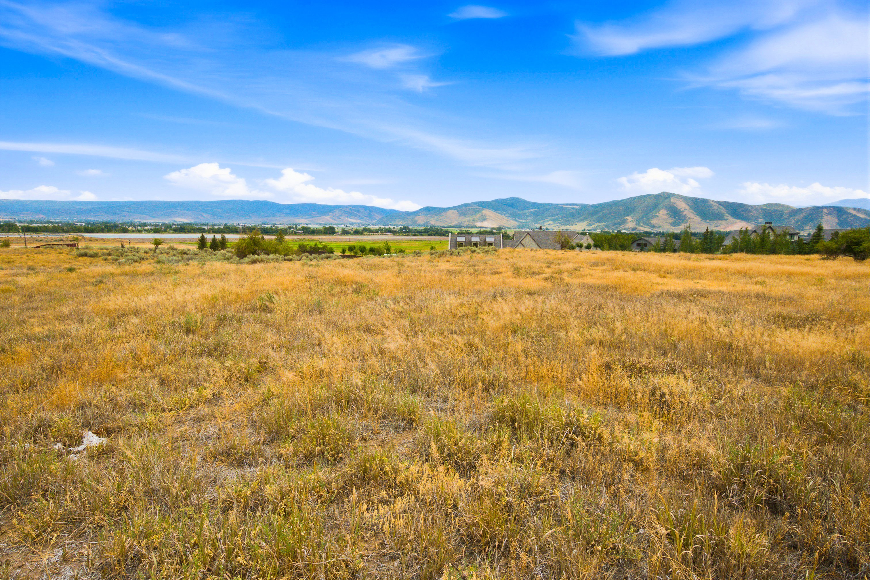 Expansive land parcel featuring natural grasses, distant mountains, and scattered residential properties
