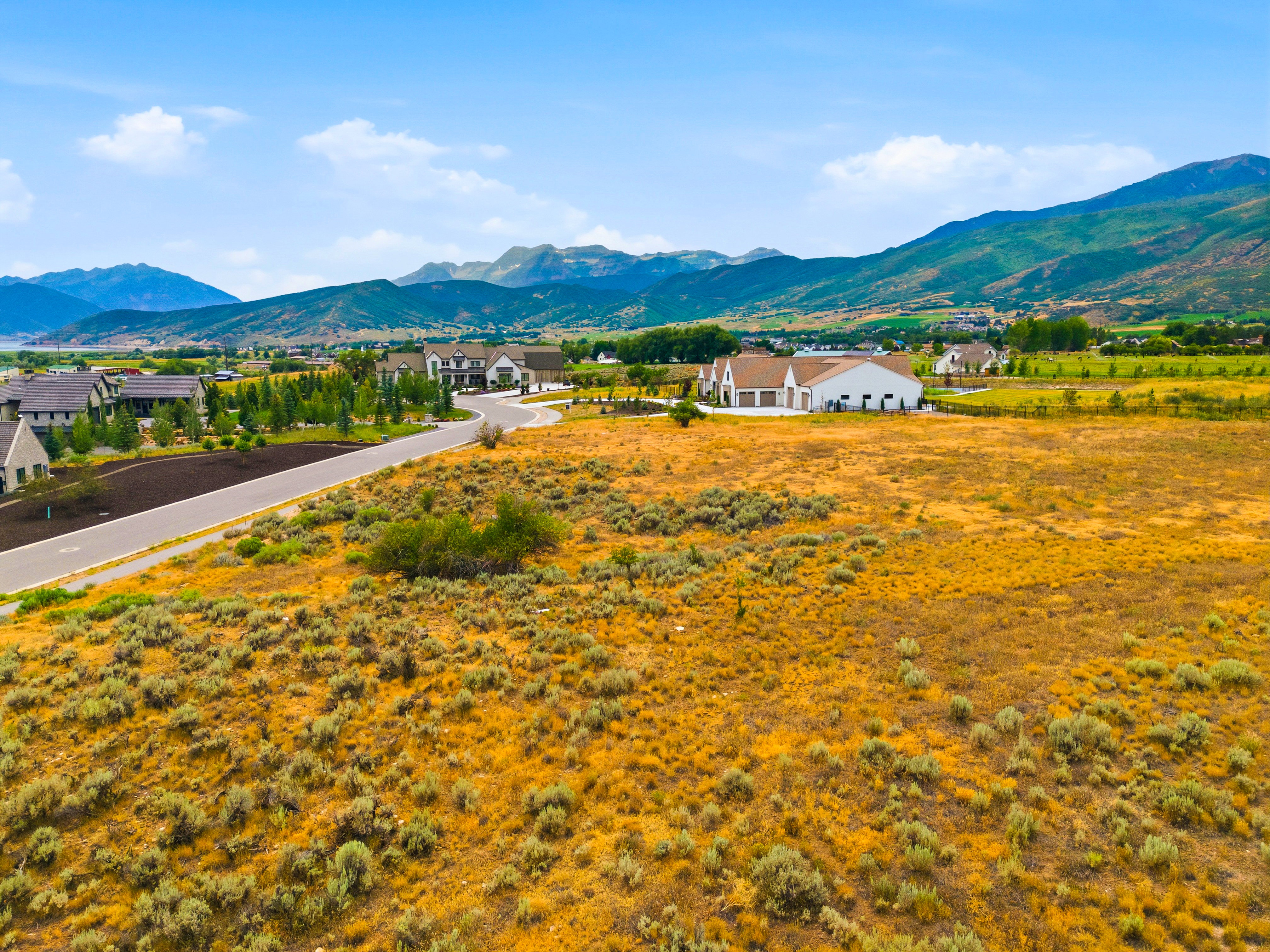 Expansive undeveloped lot featuring natural shrubbery and a clear sky, with mountain ranges forming the distant backdrop
