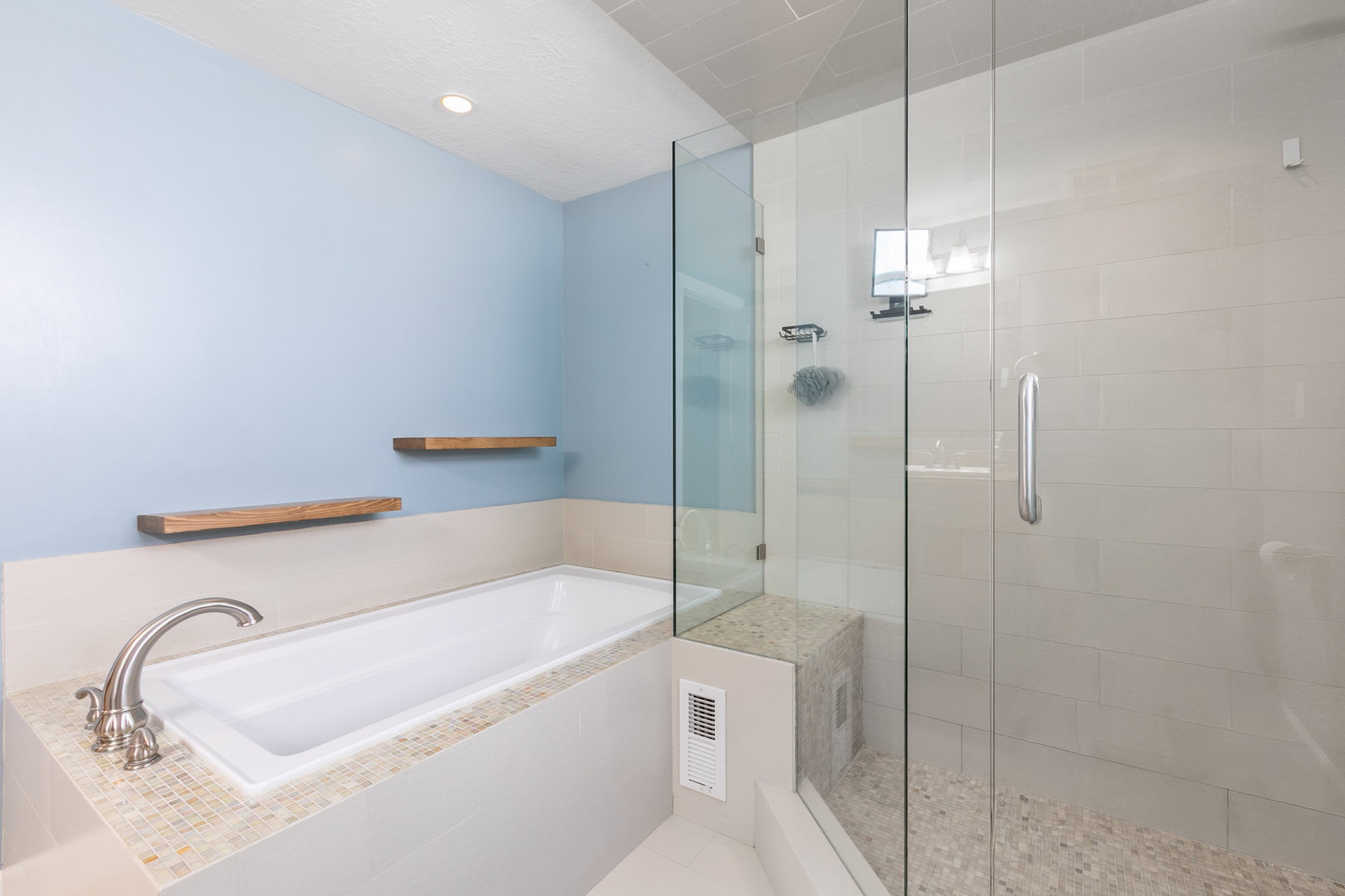 Contemporary bathroom featuring a built-in tub with brushed nickel fixtures, glass-enclosed shower with a bench, light-toned wall tile, and pebble-finish shower floor