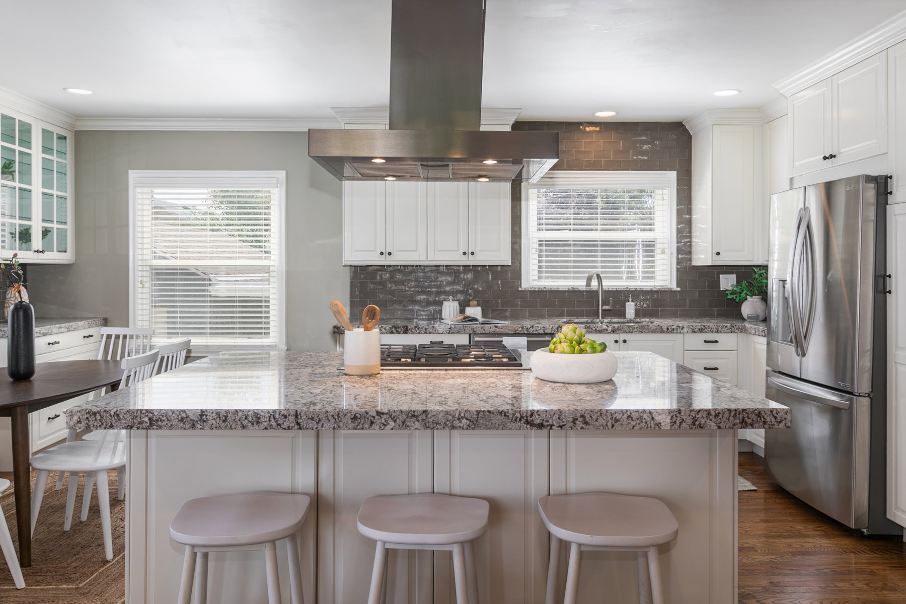 Kitchen featuring a large island with a gas range, stainless steel appliances, white cabinetry, and a dark tile backsplash