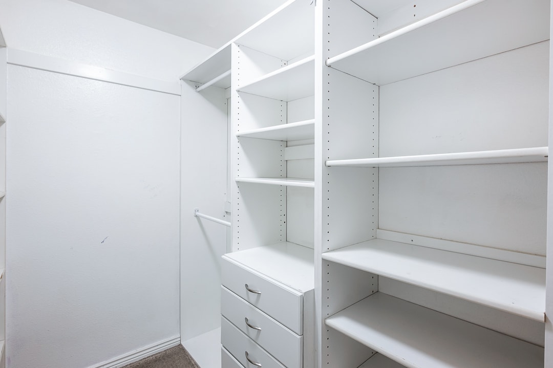 Walk-in closet featuring white built-in shelving, multiple hanging rods, and integrated drawers with chrome hardware