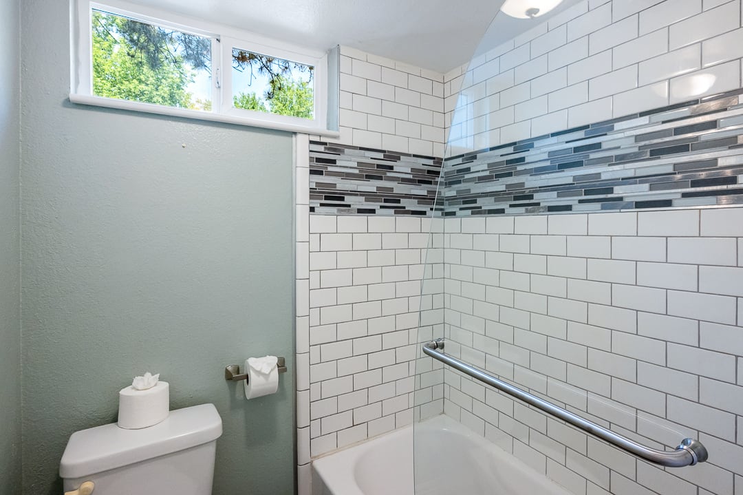 Bathtub and shower combination featuring white subway tile surround with a decorative mosaic accent band